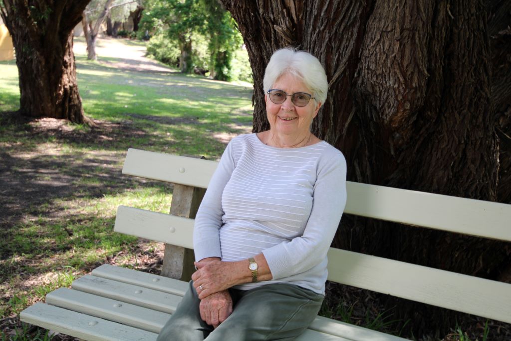 A lady smiles and sits on a bench in the park.